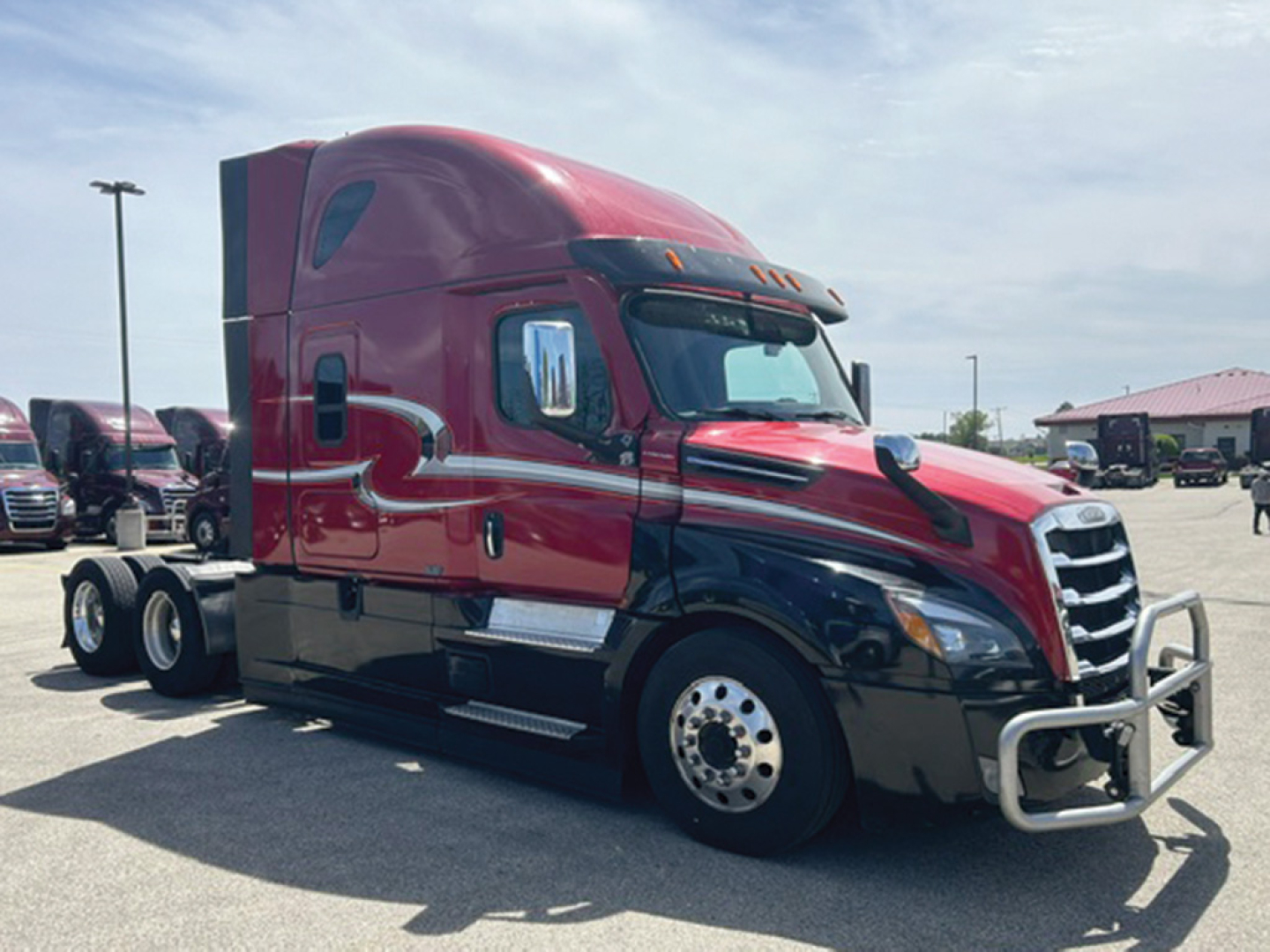 Freightliner Cascadia126 sleeper cab tractor in red and black, side view showing chrome bumper guard and dual rear axles.