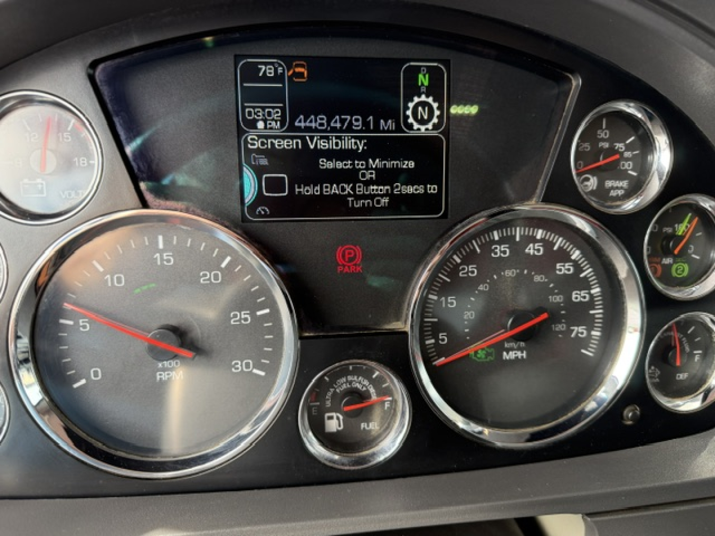 Dashboard of a Kenworth truck showing multiple gauges, digital display, and warning icons. Text on screen includes 'Screen Visibility: Hold BACK Button to Turn Off' and '448,479.1 MI' plus various gauge markings.