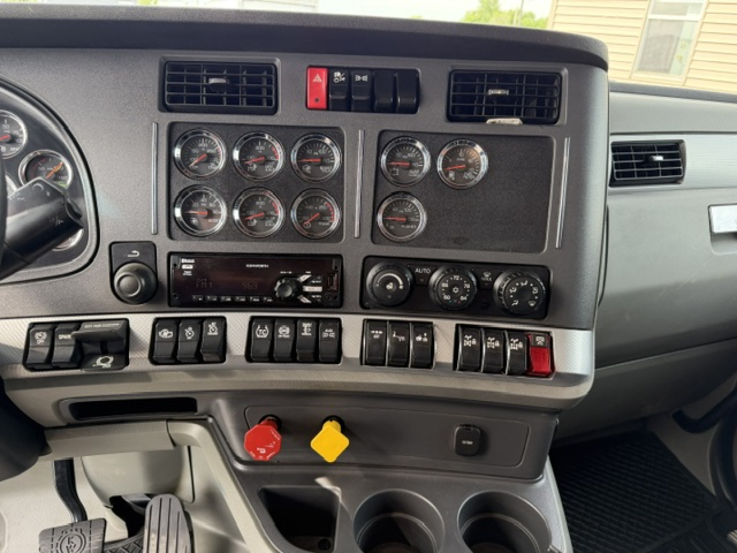 Kenworth T880 dashboard with multiple gauges and controls in view, center console with switches, two cup holders, red and yellow knobs visible.