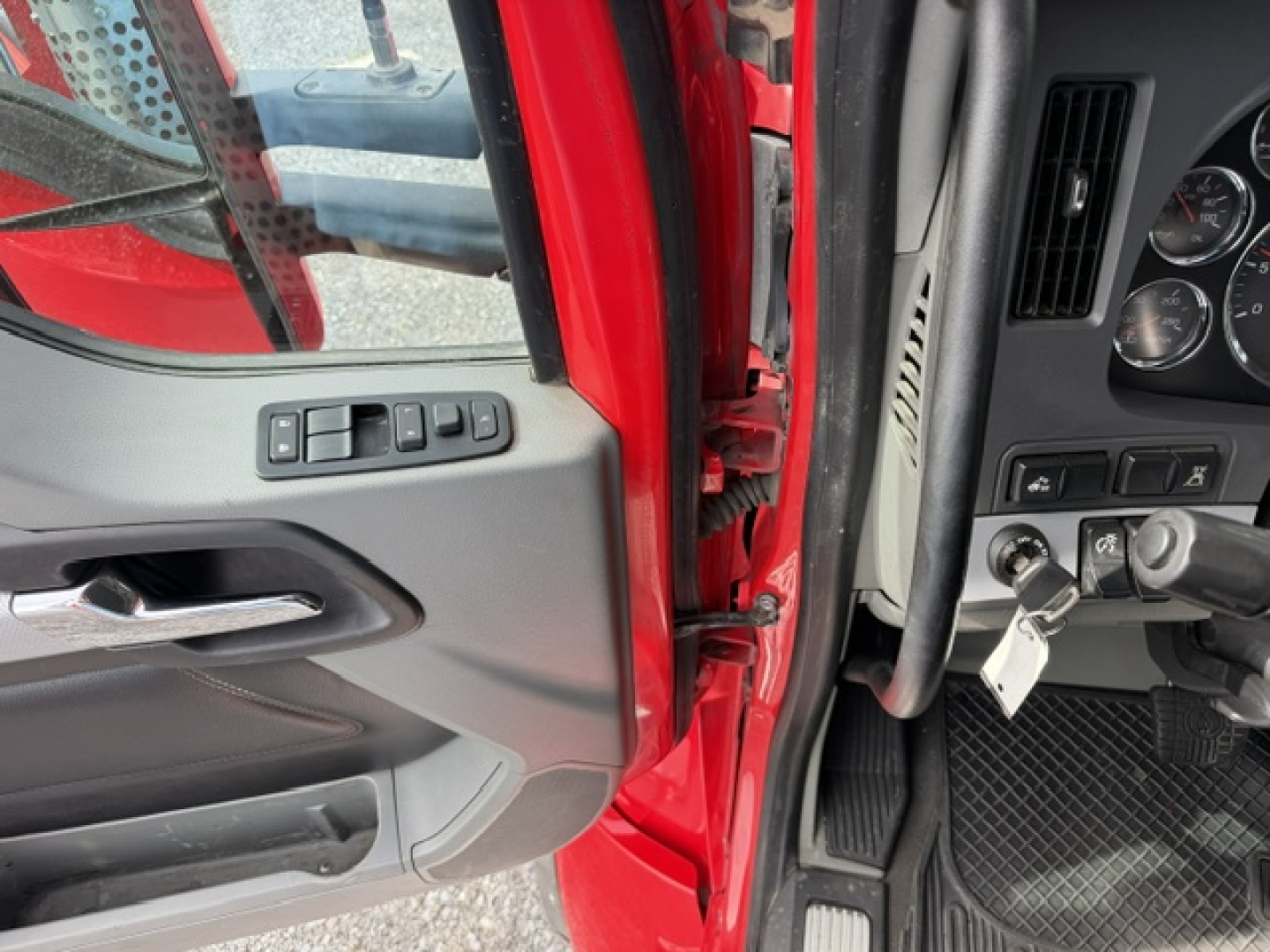Truck cab interior showing door panel and dashboard with ignition keys; red paint visible at door frame; control switches on door and instrument cluster with gauges.