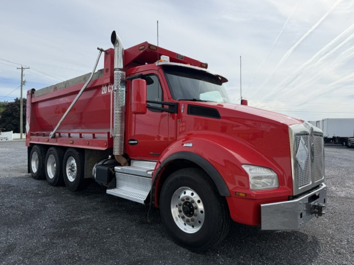 Kenworth T880 dump truck in red shown from a side angle with triple rear axles and chrome exhaust stack.