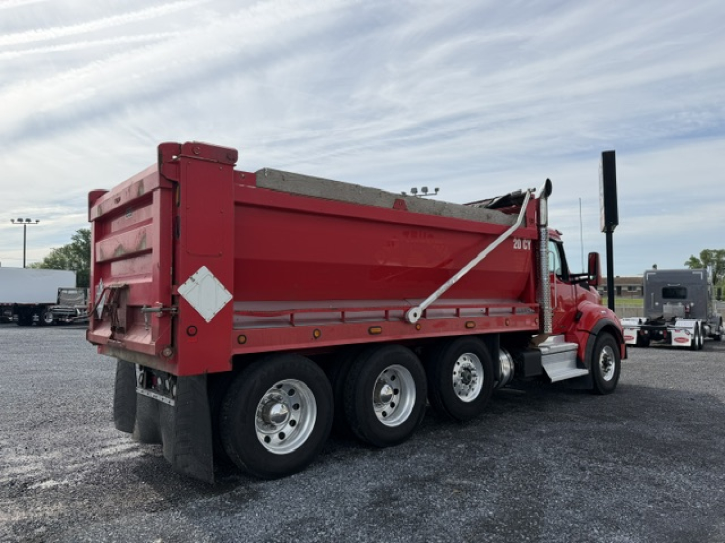 Kenworth T880 dump truck in red, side and rear view showing dump bed, dual rear wheels, and white reflective safety decals.