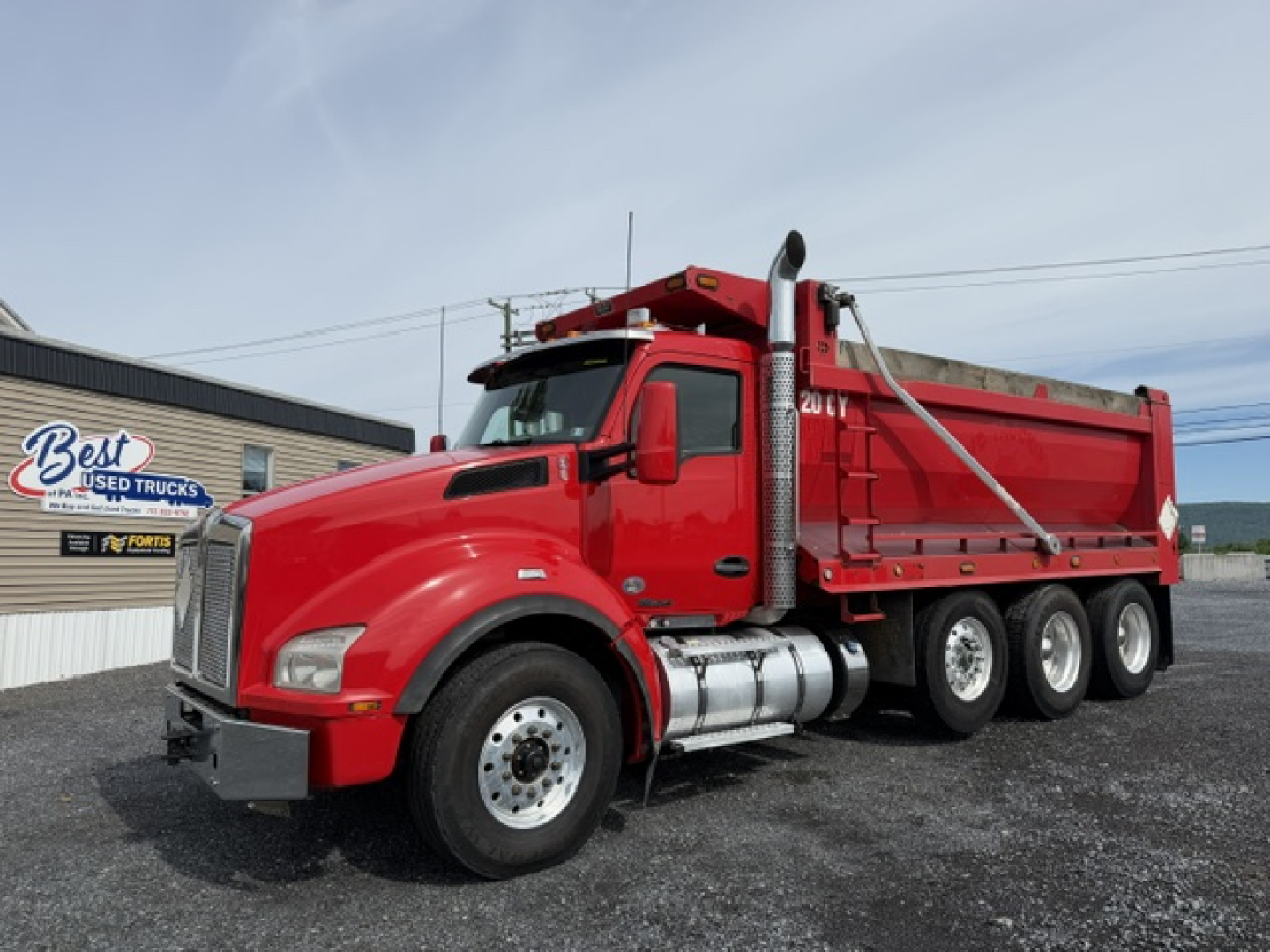 Kenworth T880 dump truck in red, side view showing cab, dual rear axles, diesel fuel tanks, and dump bed; no legible labels or text visible on the truck.