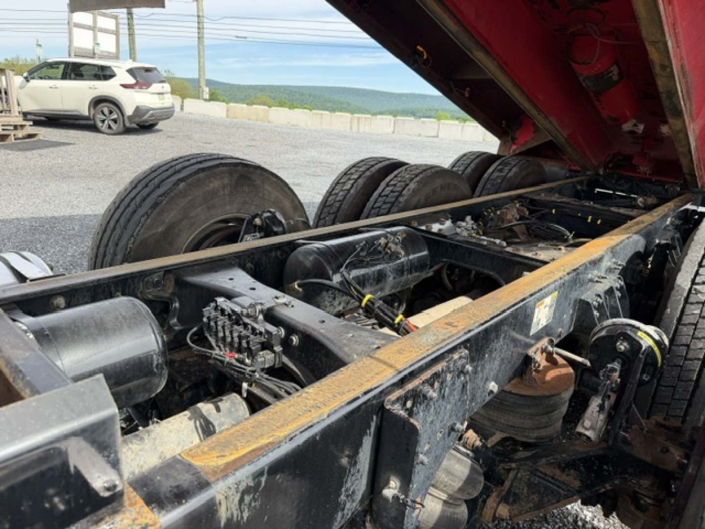 Kenworth T880 dump truck chassis with exposed undercarriage, suspension, and wheelset. Raised bed with hydraulic components visible, drums, tubing, and wiring loom.