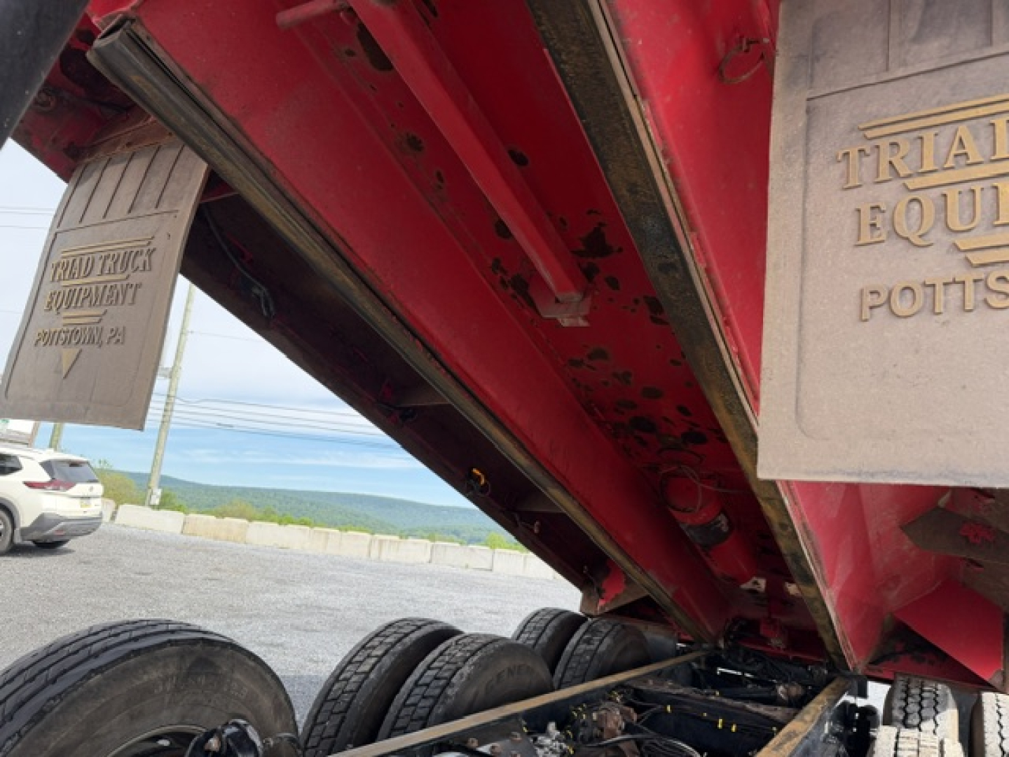 Kenworth T880 dump truck undercarriage showing red frame and dual rear axles with tires and a metal plate with embossed text.