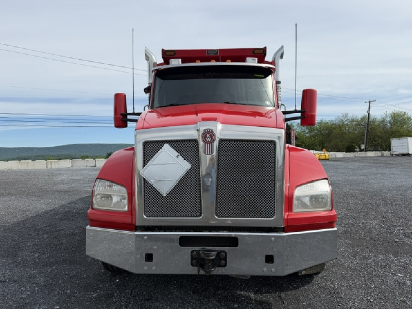 Kenworth T880 front view dump truck with red cab, chrome grille, and large bumper. Text not clearly visible on badges.