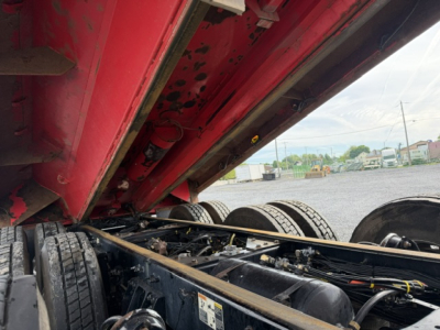 Kenworth T880 truck dump chassis view with raised red bed showing dual rear axles and fuel tanks.