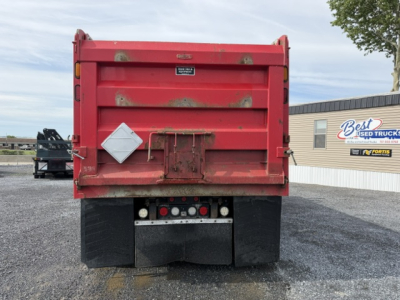 Rear view of red Kenworth T880 dump truck bed with diamond-shaped hazard placard, rear lights, and mud flaps visible.