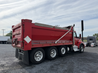 Kenworth T880 dump truck in red, side and rear view showing dump bed, dual rear wheels, and white reflective safety decals.