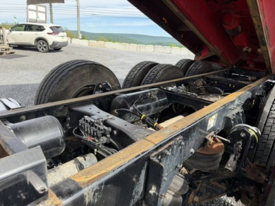 Kenworth T880 dump truck chassis with exposed undercarriage, suspension, and wheelset. Raised bed with hydraulic components visible, drums, tubing, and wiring loom.