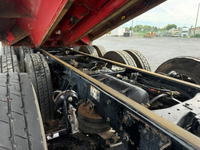 Kenworth T880 dump truck chassis under raised bed showing rear wheels, suspension, and frame with hydraulic components and cylinders.