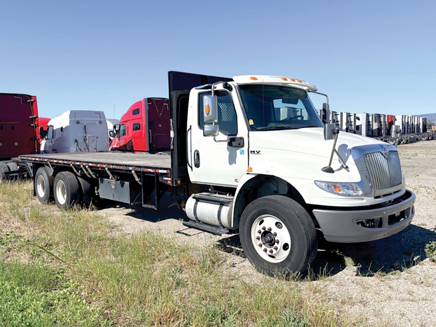 Truck: 2022 International MV607 conventional daycab with white cab and flatbed trailer, parked on grass.
