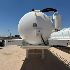 White cylindrical vacuum trailer tank with rear access hatch and hoses. Front view shows circular tank, black hose, valve, and small blue rope. Brand sticker on tank.