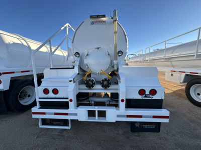 Rear view of a white Dragon 130BBL vacuum trailer showing circular tank with hoses and rear bumper lights.