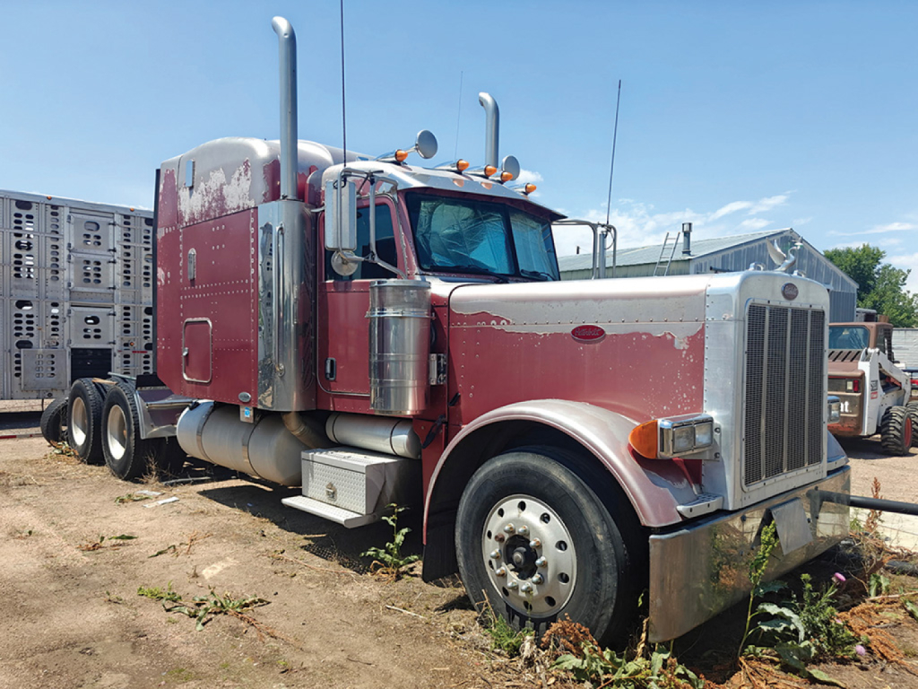 Peterbilt 379 UltraCab extended hood truck in an outdoor lot, red and tan paint, chrome grille, large dual rear wheels, exhaust stacks, side storage box, and steps.