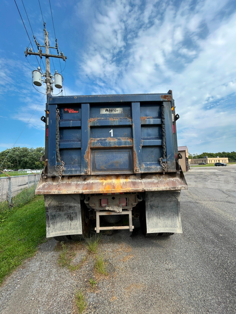 Rear view of a blue Western Star 4700 dump truck with a rusted bed and tailgate, number 1, dirt and wear on the bumper area.