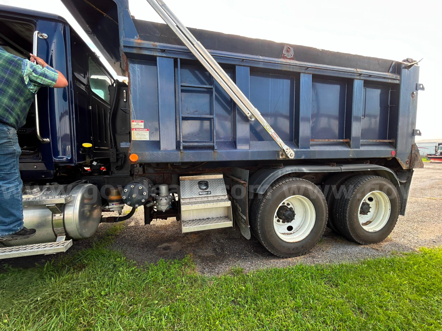Wester Star 4700 dump truck side view showing dual rear axles and blue dump bed with metal steps and fuel tank.