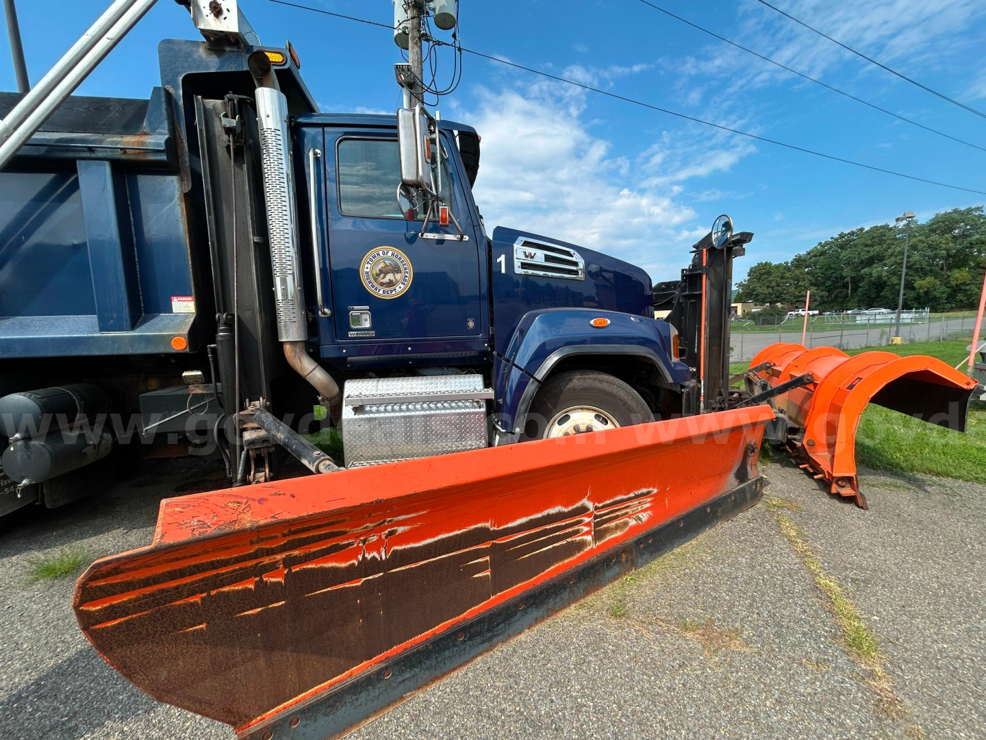 Blue 2018 Western Star 4700 plow truck with an orange snow plow blade detached, side view showing the cab and chrome exhaust stacks.