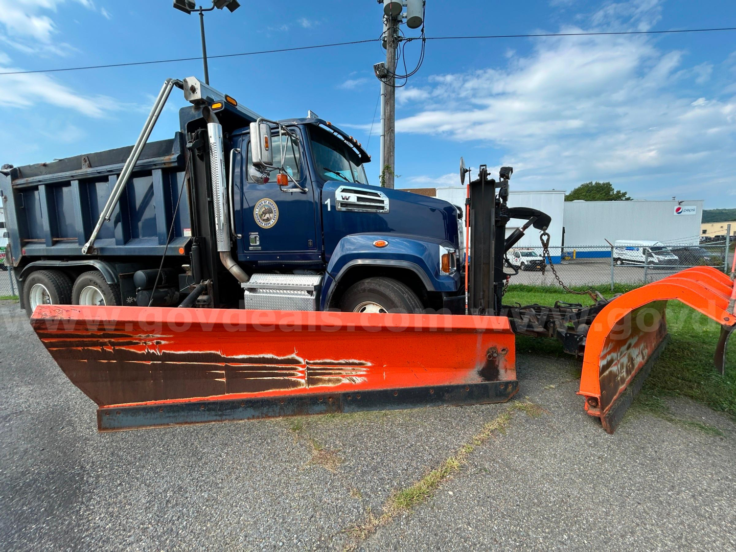 Western Star 4700 plow truck in blue with orange plow blade attached, side view showing hydraulic snowplow equipment.
