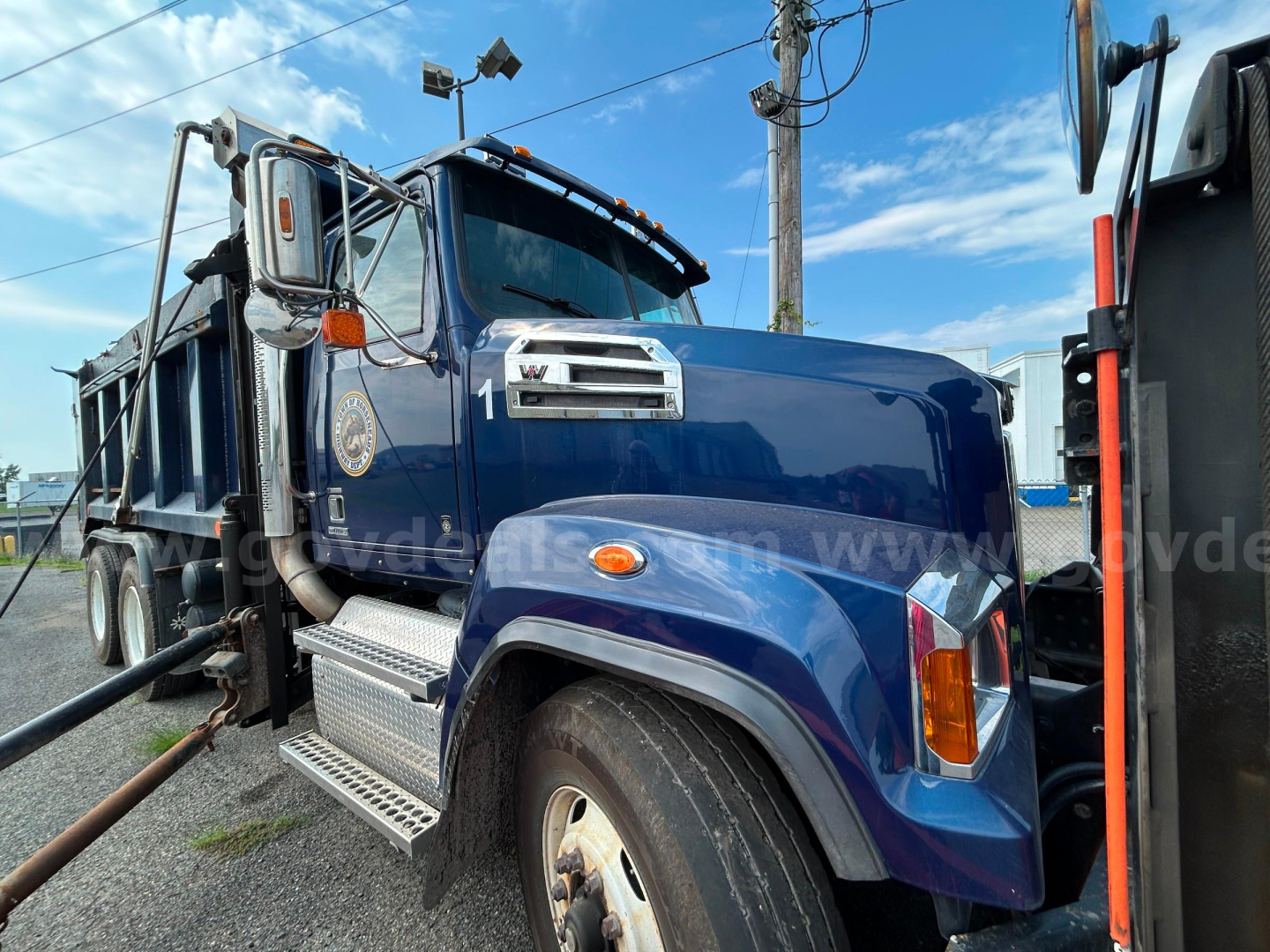 Western Star 4700 heavy-duty truck with plow attachment and blue cab, side view showing front wheel, steps, and chrome exhaust.