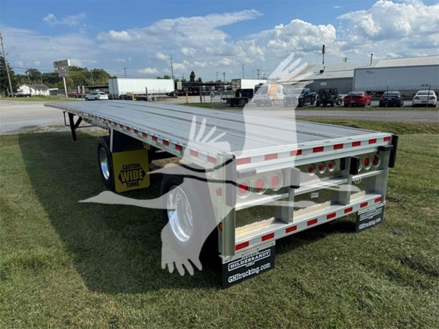 Trailer view of a 2025 Reitnouer Maxmiser flatbed trailer showing rear and side with multiple axles and red/white reflective tape.