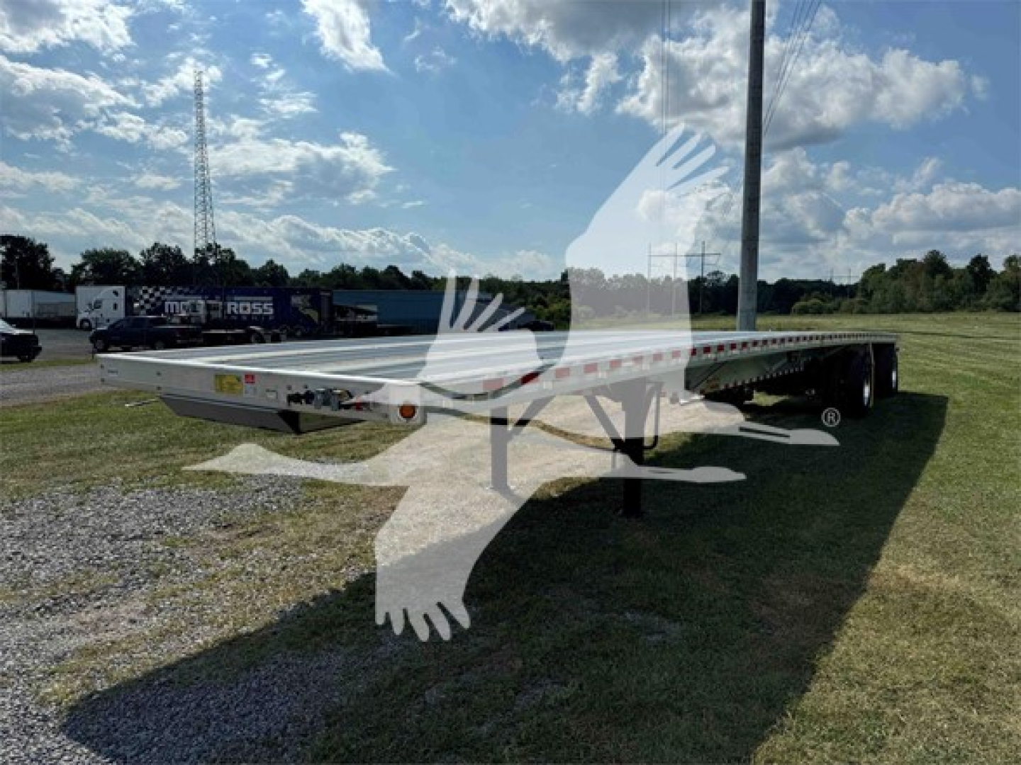 Flatbed trailer showing long aluminum deck and tandem axles with support legs, 2025 Reitnouer Maxmiser branding, parked on grass.