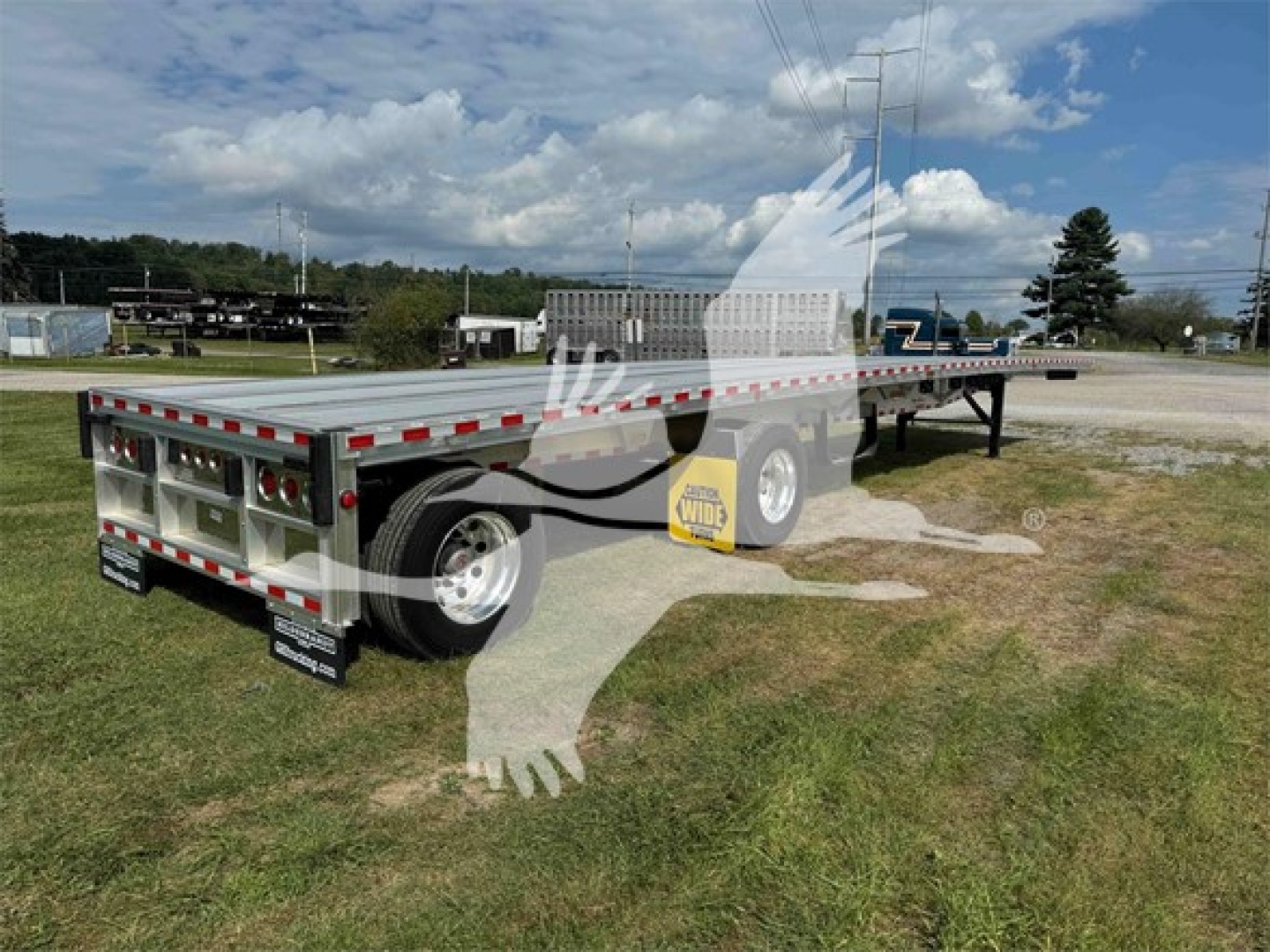 Flatbed trailer showing dual rear axles and long deck with aluminum side rails and red reflectors.