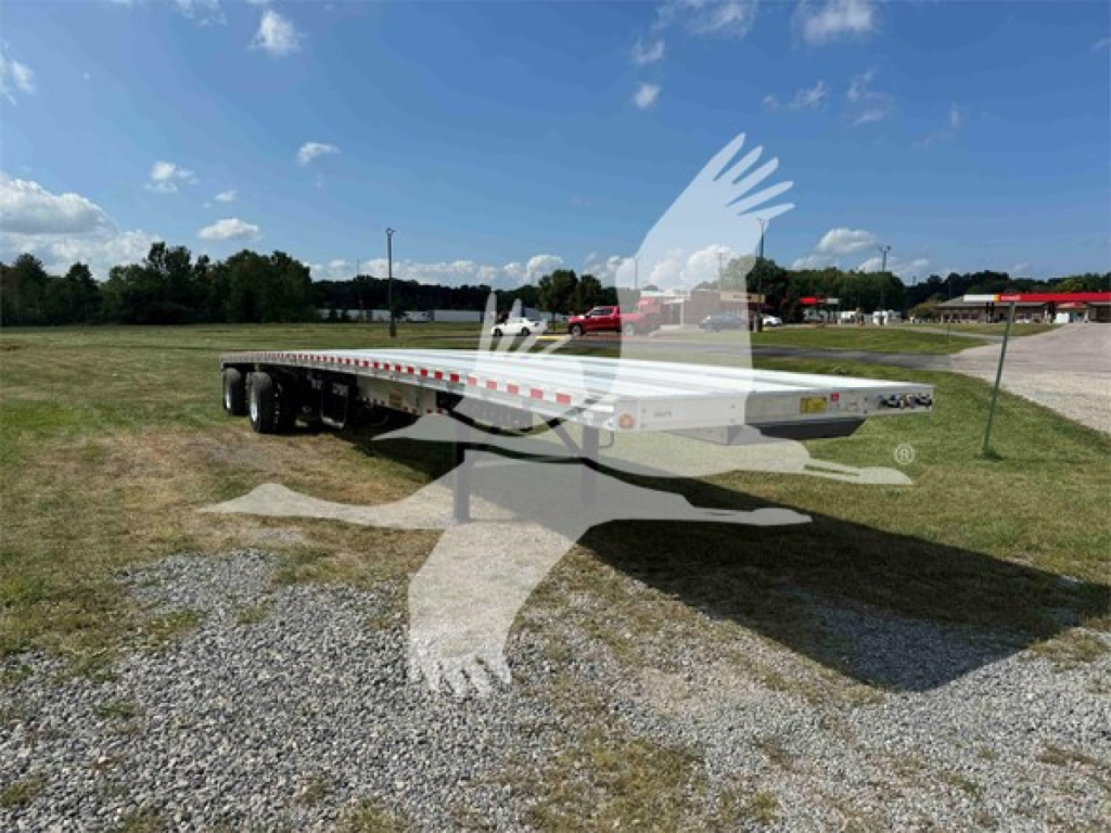 Flatbed trailer in a field showing a low-angle view with dual rear axles and long flat deck for a 2025 Reitnouer Maxmiser trailer.