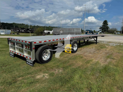 Flatbed trailer showing dual rear axles and aluminum decking with reflective tape; rear lights and mud flaps visible; stock tag and branding on tires.