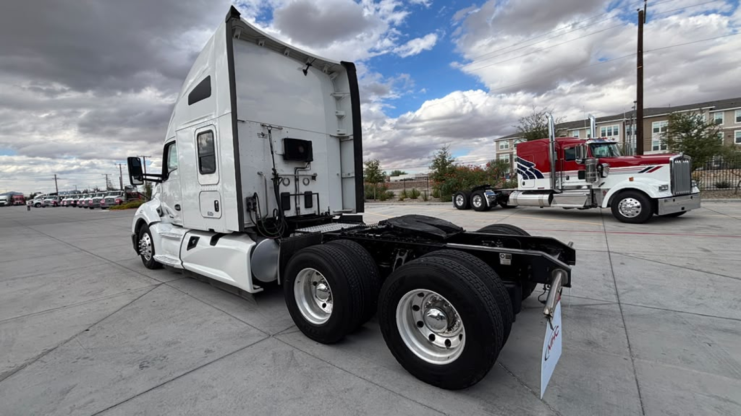 Kenworth T680 tractor cab with rear view showing dual rear axles and empty fifth wheel, white paint, visible side window, parked in lot.