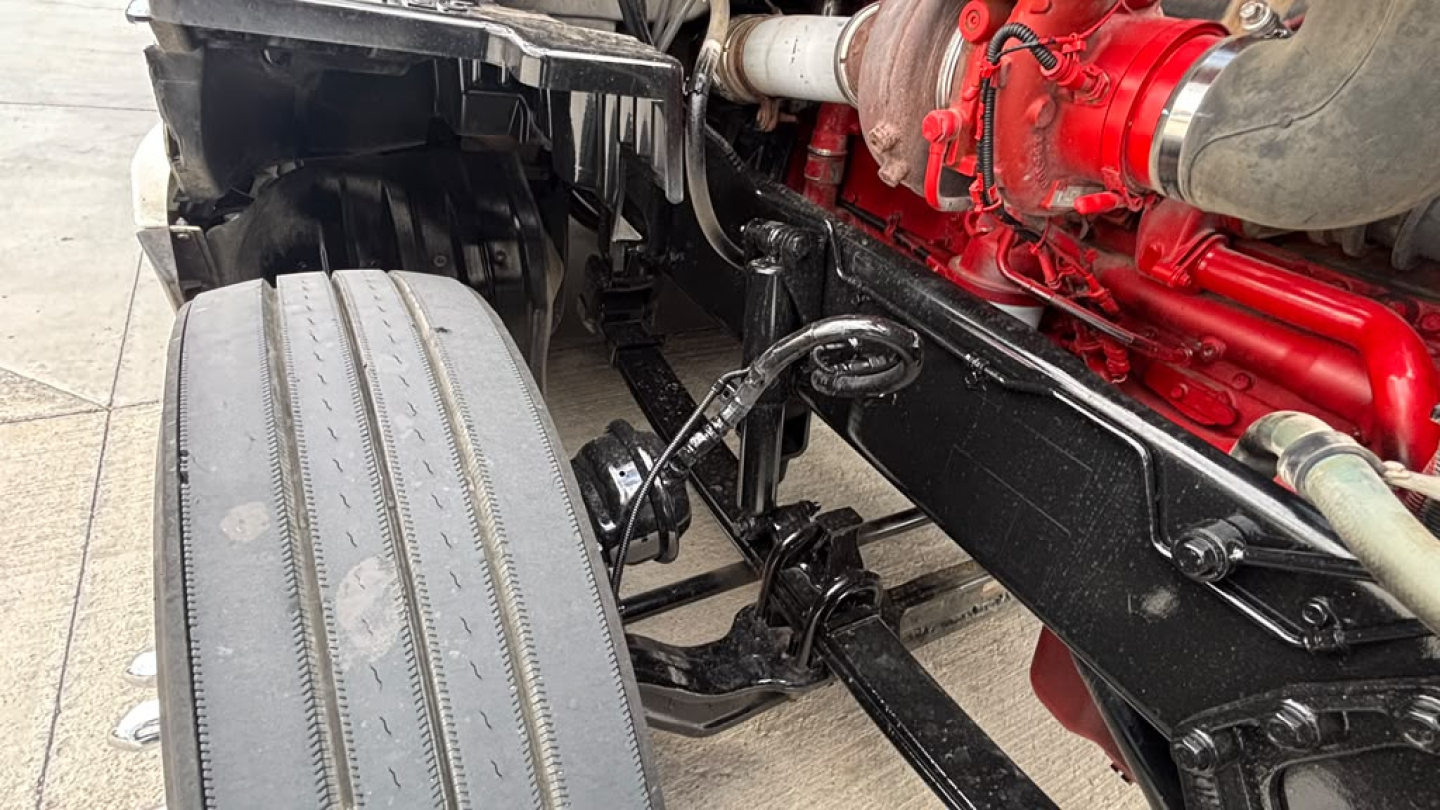 Kenworth T680 chassis showing front axle and engine with red-painted components and black frame.