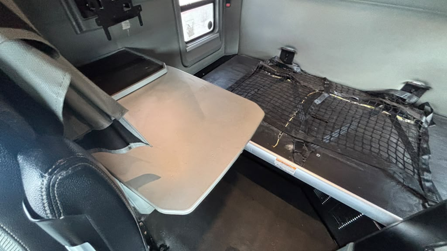 Kenworth T680 interior cargo area with foldable table and cargo net; sleeping area shown with a small table and overhead storage.