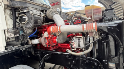Kenworth T680 engine bay with red engine block, intake tubing, hoses, and radiator components visible.