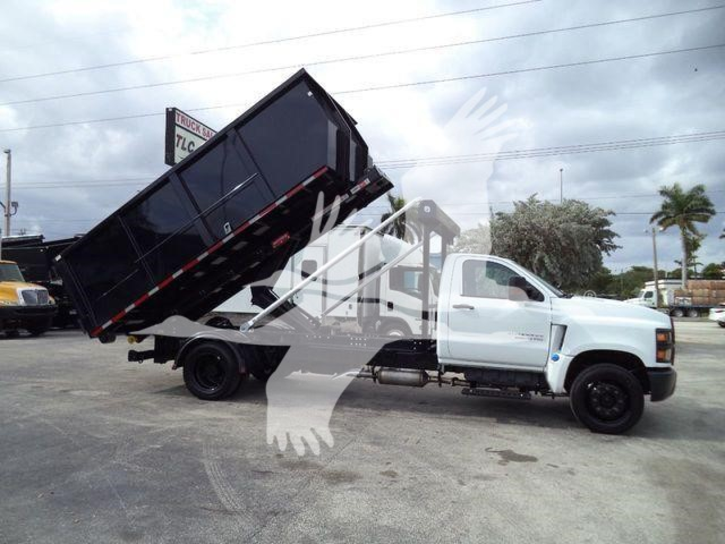 Truck side view showing a white 2023 Chevrolet Silverado 6500HD with a raised black dump bed in a dump truck configuration.