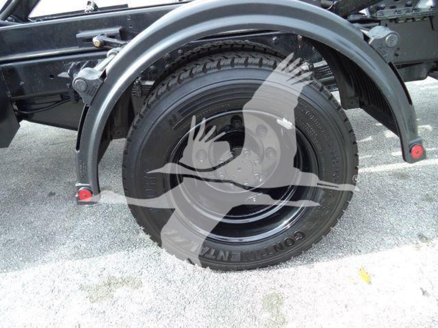Wheel well and tire of a heavy-duty truck chassis showing a mounted spare tire and fender, with rim and suspension components.