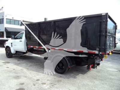 Truck bed of a 2023 Chevrolet Silverado 6500HD rolloff with black dump bed, white cab, hydraulic strap, and rear-view showing no visible branding text.