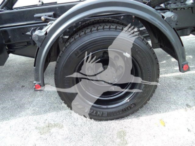 Wheel well and tire of a heavy-duty truck chassis showing a mounted spare tire and fender, with rim and suspension components.