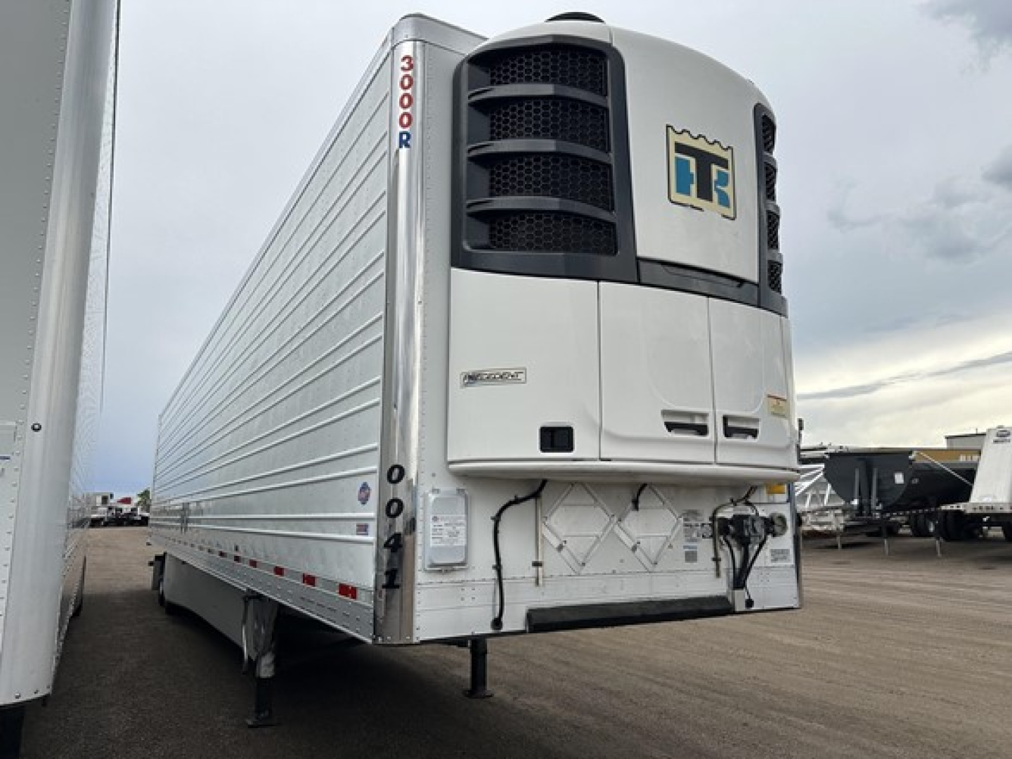 Utility 3000R trailer in side view with reefer unit at front and vertical '3000R' decal, silver mid-section, dealership lot in background.