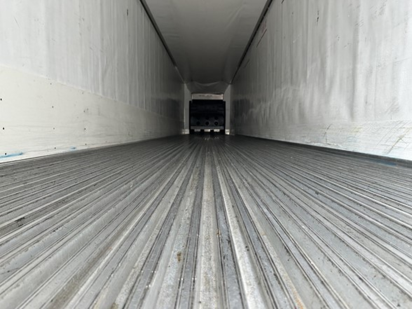 Trailer interior showing ribbed floor and side walls of a refrigerated trailer with rear doorway in view.