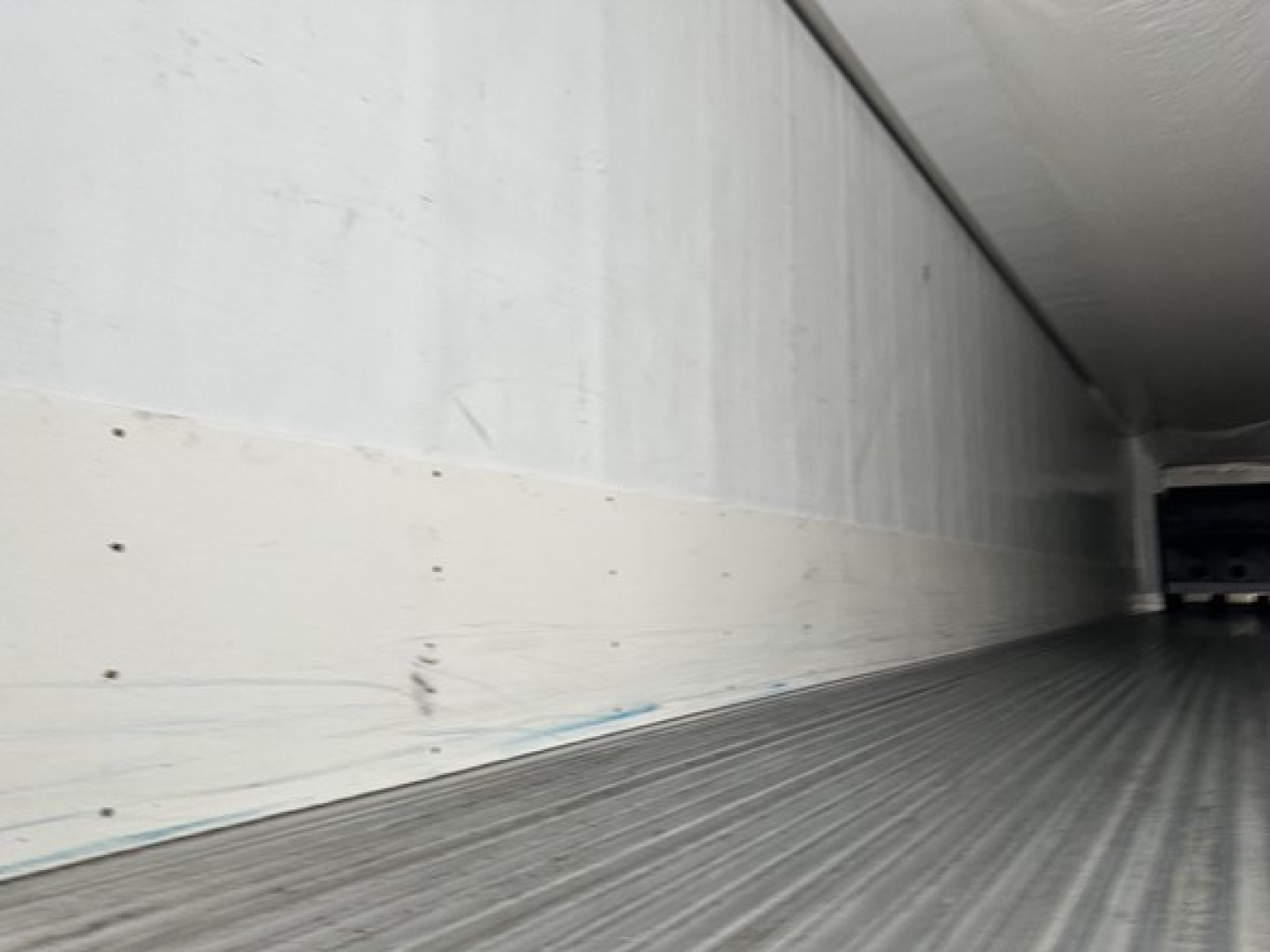 Trailer interior cargo area showing ribbed aluminum floor and side wall with light finish and rear access opening.