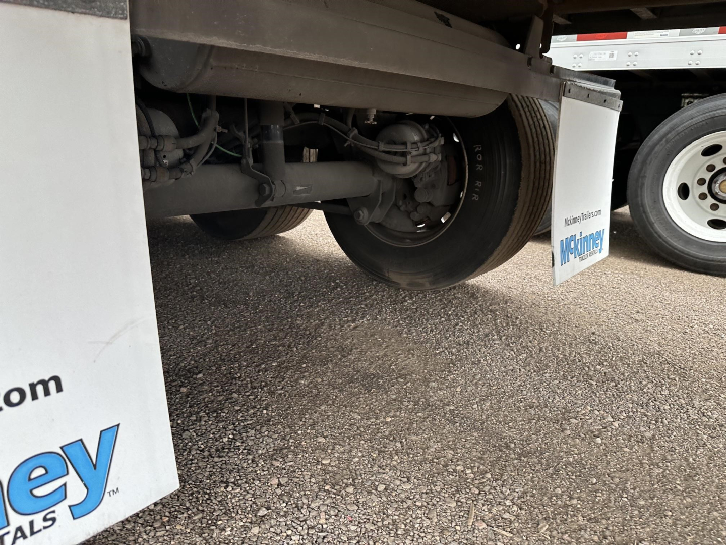 Trailer undercarriage showing wheel and suspension components with white mud flaps and branding.