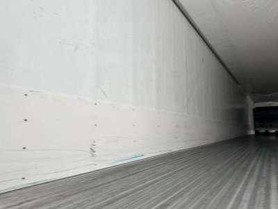 Trailer interior cargo area with corrugated metal floor and white sidewall panels, viewed from the rear.