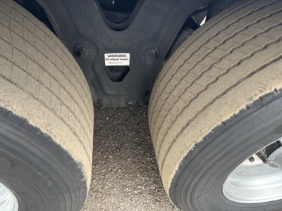 Trailer undercarriage showing dual tires and suspension with a small label reading 'LASER LINED' on the chassis. Visible part of the fifth wheel area and ground surface between wheels.