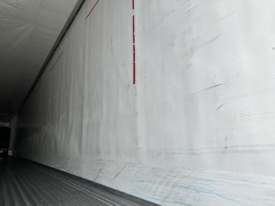 Long empty trailer interior with ribbed metal floor and white side wall, minimal markings; a red vertical line marking near front.