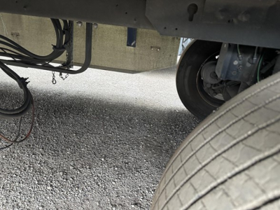 Trailer undercarriage showing wheel and suspension components with exposed wiring and hoses.