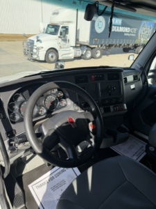 Kenworth T680 interior view showing steering wheel and dashboard while parked; exterior trailer visible through windshield with Diamond Kote trailer paint.