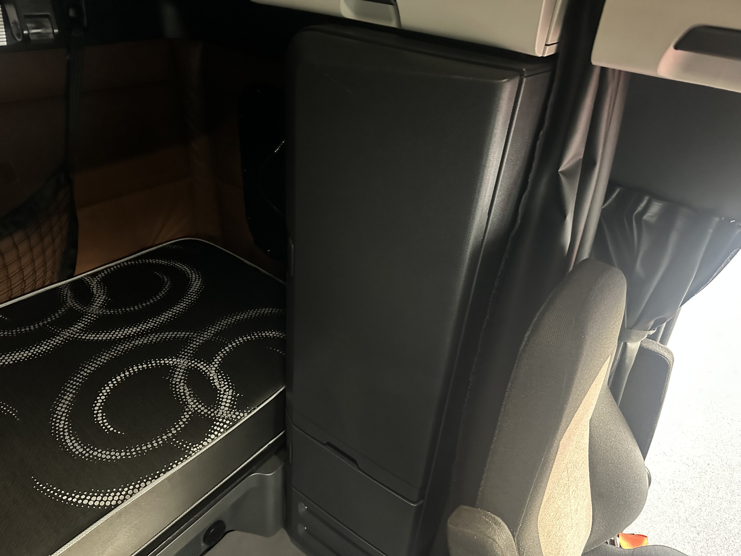 Cab interior of a 2022 Freightliner Cascadia 126 sleeper showing driver's seat and storage compartment, limited view of bunk area.