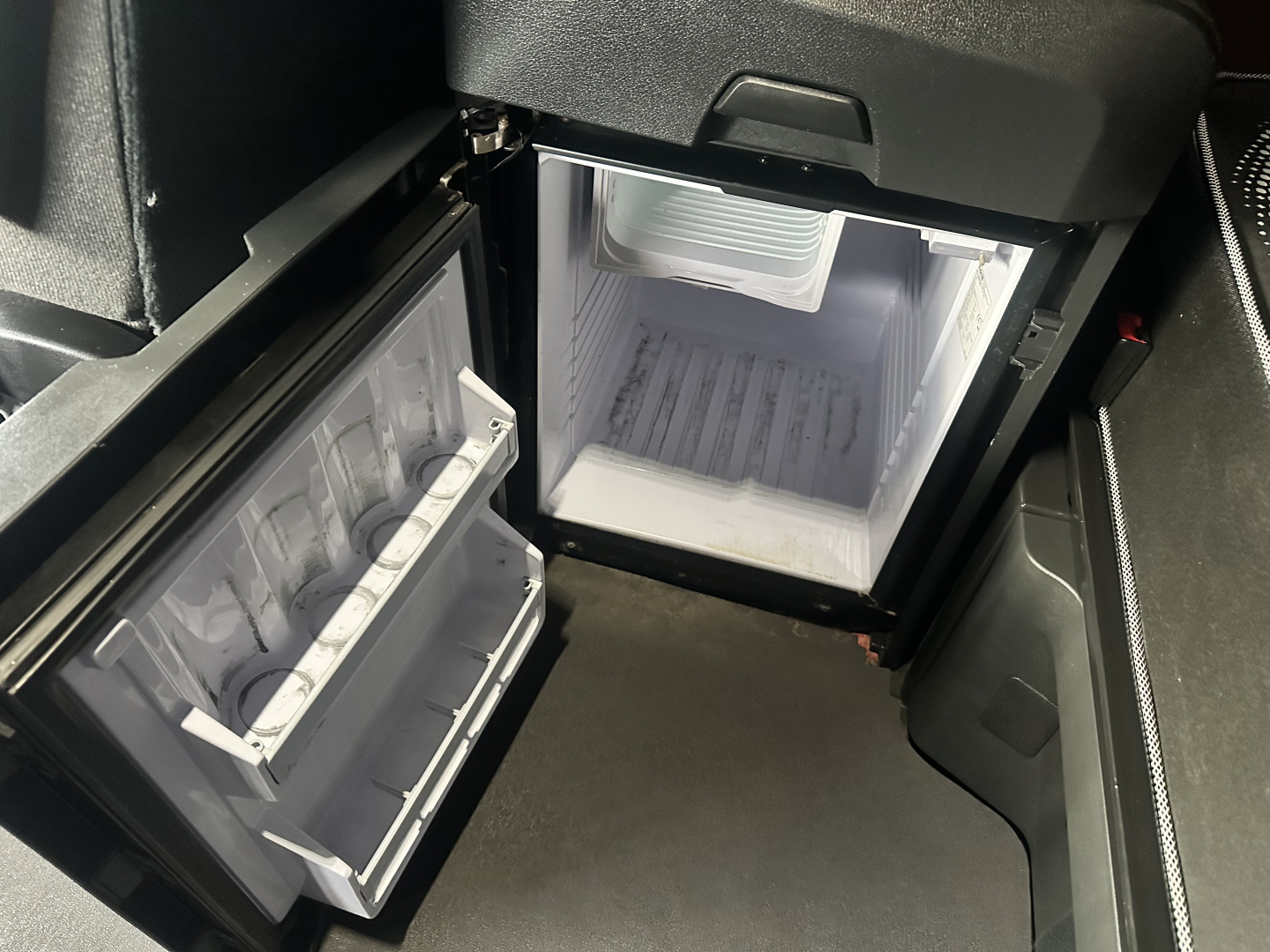 Freightliner Cascadia 126 cab interior showing open small fridge/freezer with shelves and a compact fridge in the cab, compact freezer unit and interior storage.