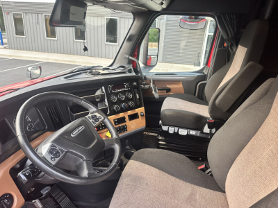 Cab interior of a Freightliner Cascadia 126 truck showing steering wheel, dashboard with gauges, center console, and driver seat.