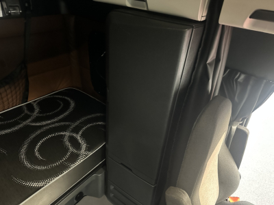 Cab interior of a 2022 Freightliner Cascadia 126 sleeper showing driver's seat and storage compartment, limited view of bunk area.